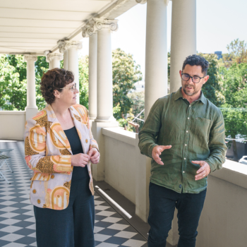 Two people in conversation on a heritage building's colonnaded verandah.